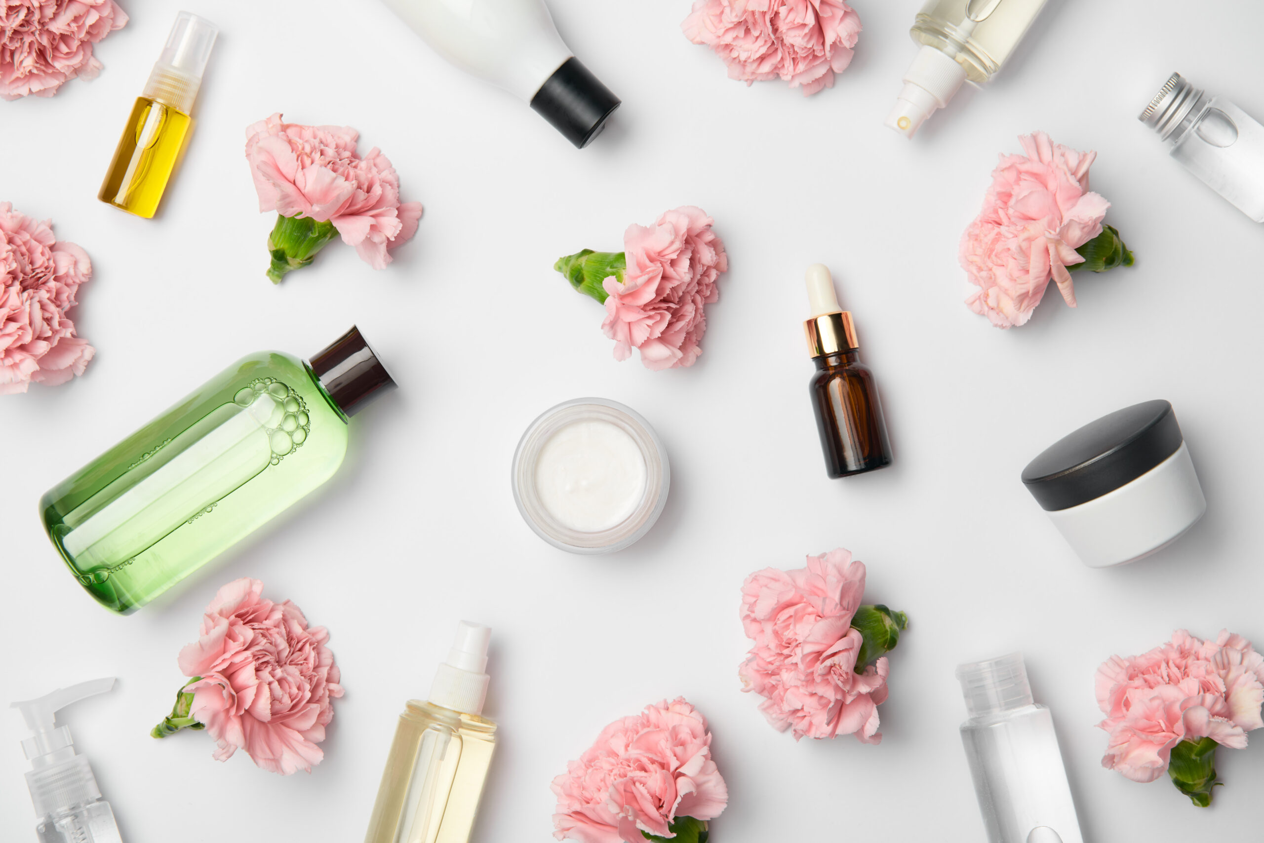 Top view of various cosmetic containers and pink carnations flowers on white background